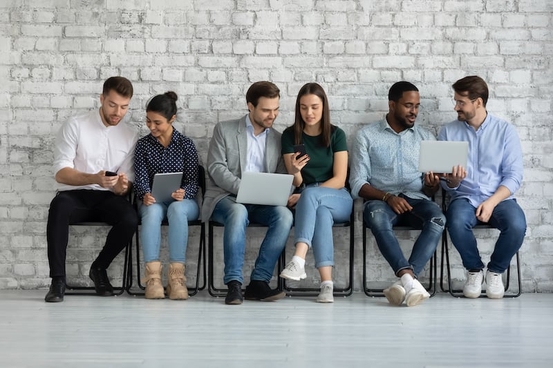 Diverse group of young people sitting on devices against a wall