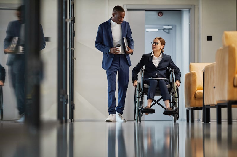 Woman wearing a suit in a wheelchair with a man in a suit walking next to her