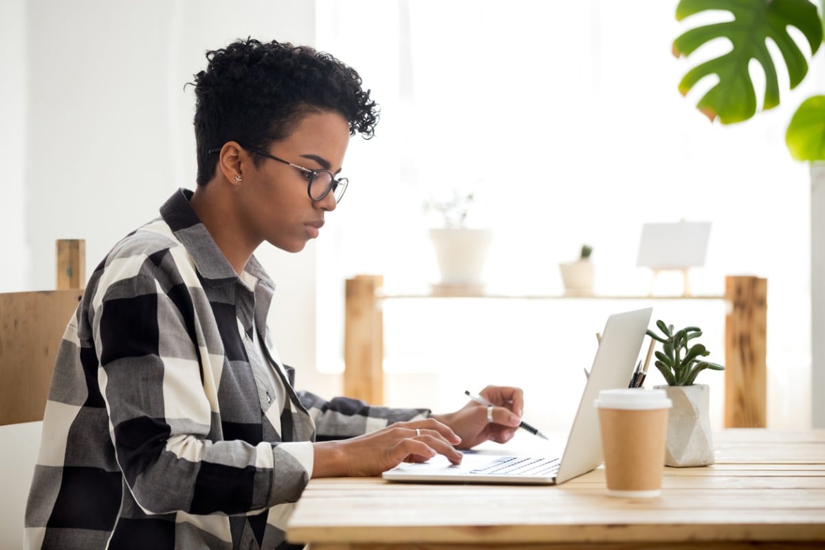 Young person looking at a laptop with pen in hand