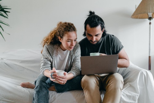 A couple sitting on couch looking at a laptop screen together