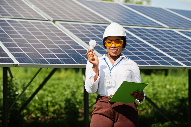 Woman standing in front of solar panels with a lightbulb in her hand