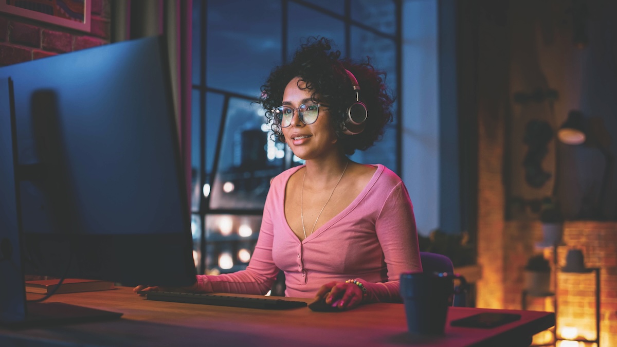 Young black woman wearing glasses and sitting in front of a computer in low light