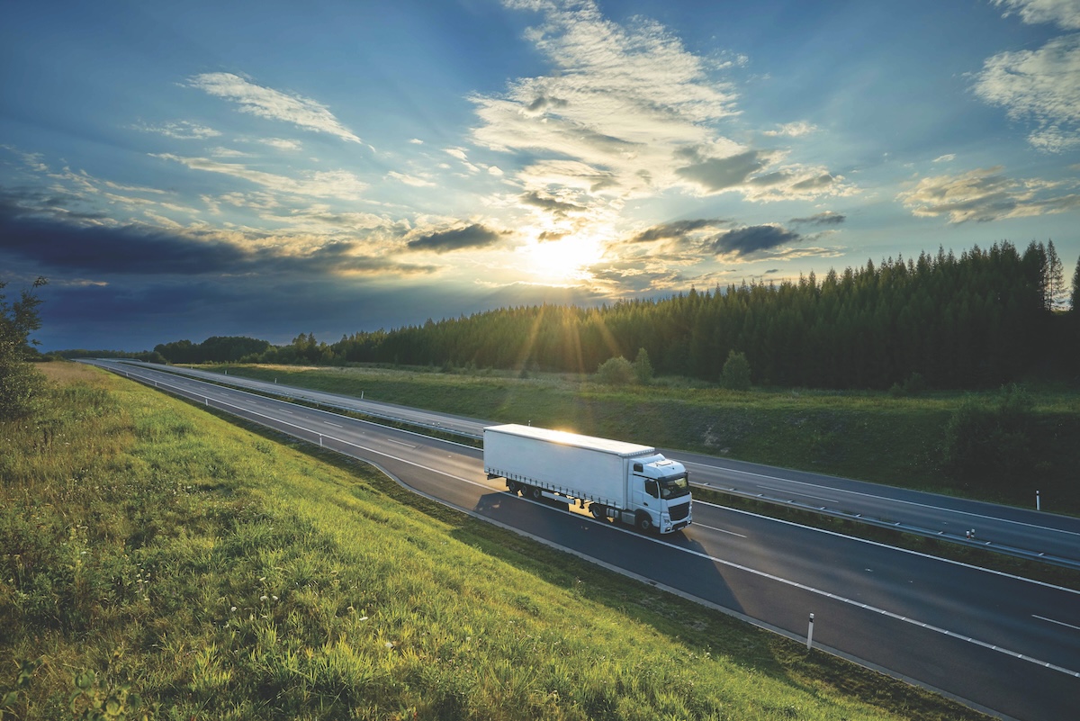 A freight truck driving on a highway the sun setting in the background