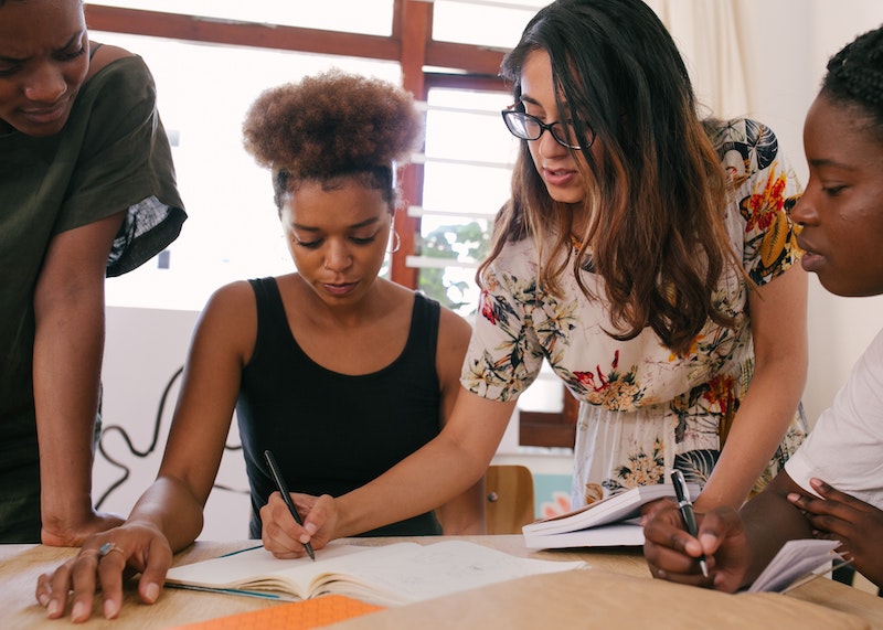 Women standing and sitting around a table looking at a document